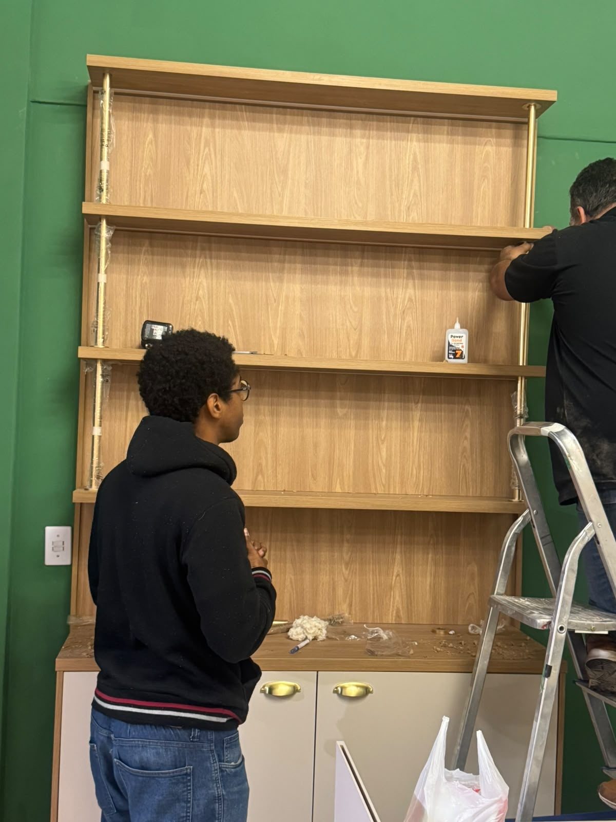 Equipe finalizando a montagem da prateleira na parede verde
