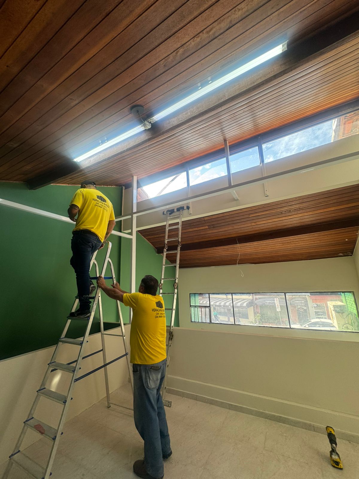 Equipe instalando elétrica — verde e forro de madeira ao fundo