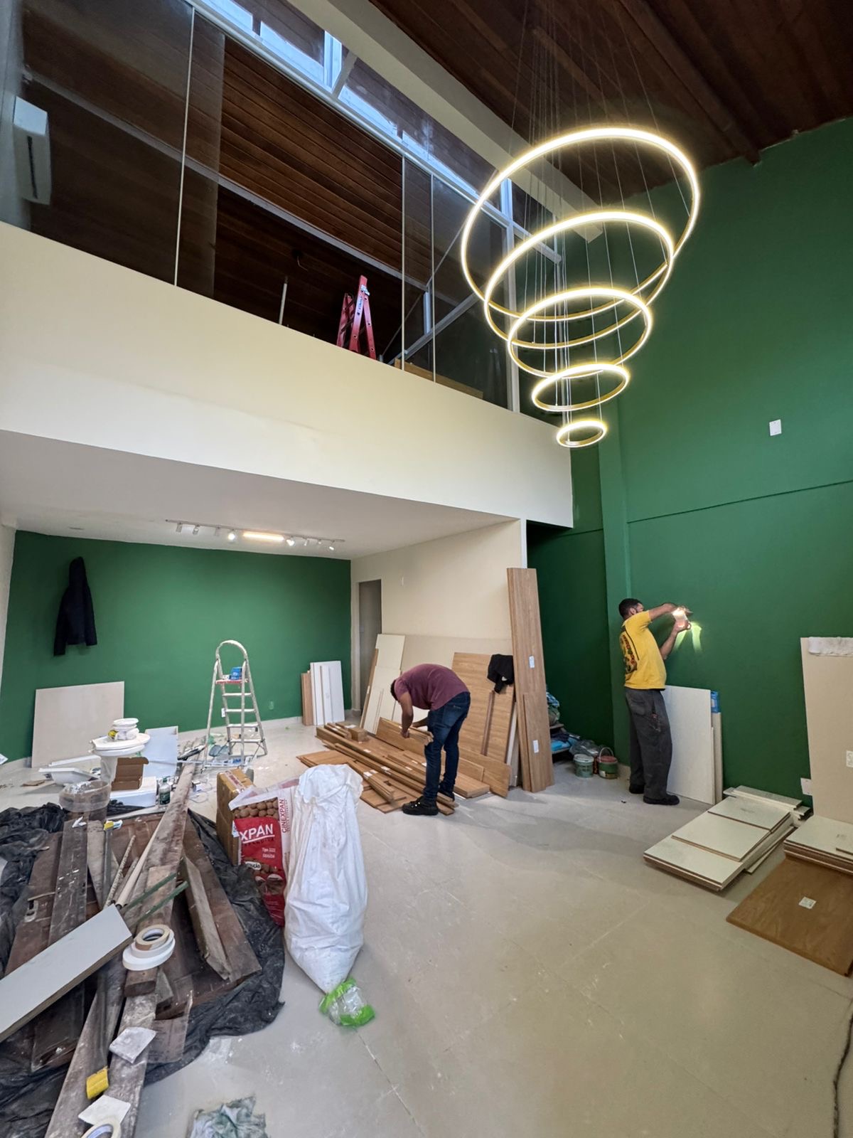 Salão com o lustre de aros já aceso e equipe trabalhando nos acabamentos