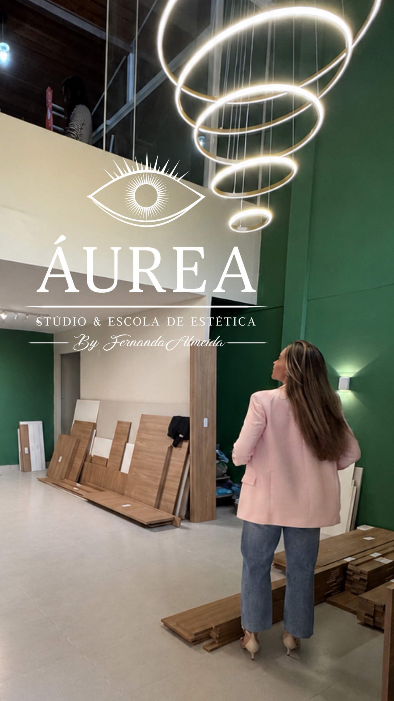 Fernanda observa o lustre de aros suspensos sob a marca Áurea, com amostras de piso de madeira ao fundo